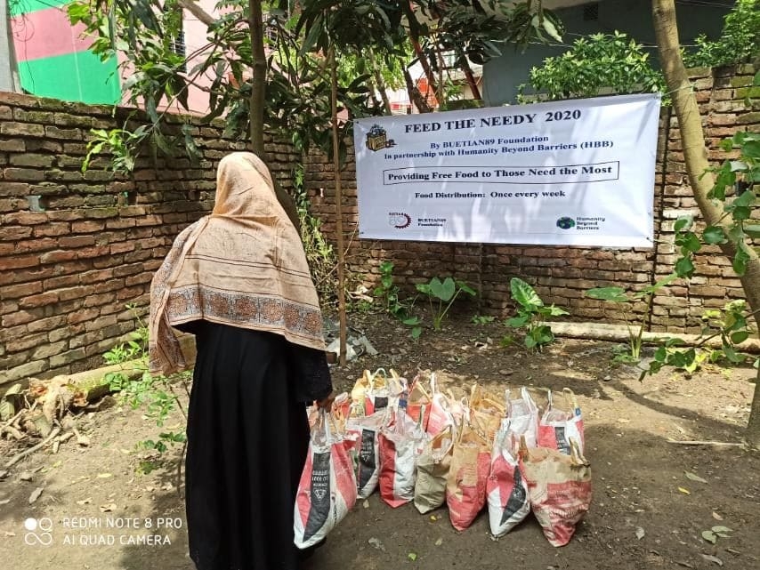 A community member beside food supplies and a project banner